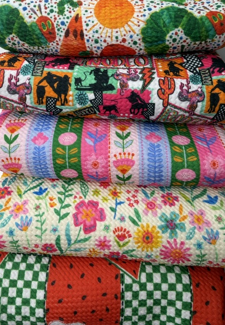 Stack of folded bullet liverpool knit fabric bolts in bright watermelon check, western rodeo, folk floral and ditsy flower prints