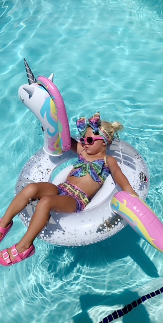 Little girl floating on a unicorn pool float wearing a handmade colorful two-piece swimsuit and matching head wrap sewn from swim spandex