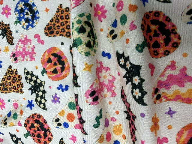 100% woven quilting cotton fabric draped in a Halloween print with jack-o-lanterns, ghosts, daisy bats and leopard pumpkins on cream