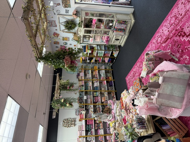 Wide view of the Blush & Bloom fabric studio floor in Branson, Missouri with a pink rug, floral fabric installations and rolls of cotton and knit yardage