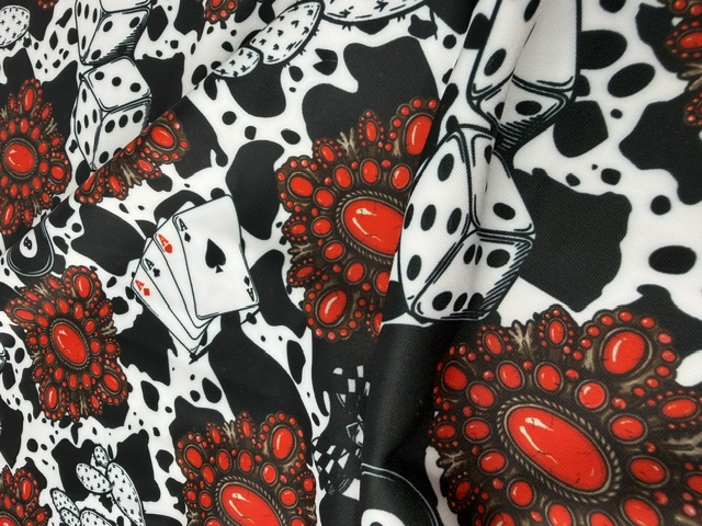 Four-way stretch spandex fabric draped in a black and white cow print with red squash blossom jewels, playing cards and dice