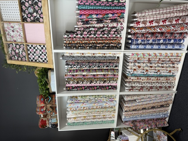 Wall shelving filled with fabric bolts beside a bright window display inside the Blush & Bloom boutique in Branson, Missouri